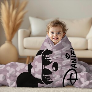 May include: A child wrapped in a lavender blanket featuring a black Mickey Mouse design and white polka dots. The blanket has the name "Daniel" printed on it, along with the Disney logo.