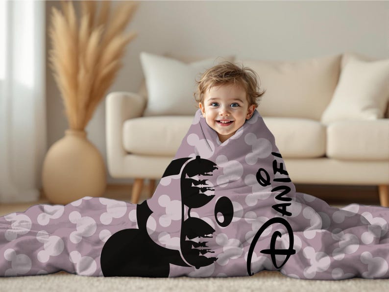 May include: A child wrapped in a lavender blanket featuring a black Mickey Mouse design and white polka dots. The blanket has the name "Daniel" printed on it, along with the Disney logo.