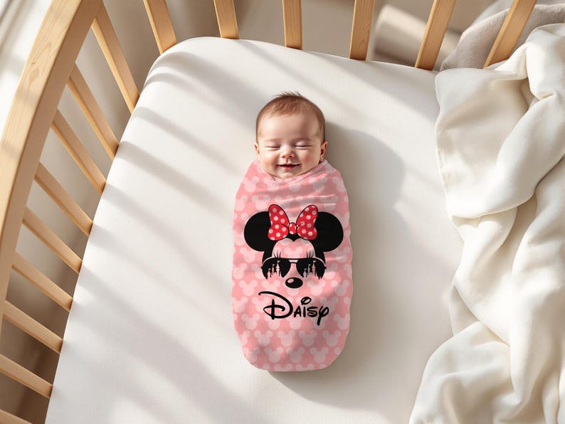 May include: A baby wrapped in a pink swaddle blanket with a Minnie Mouse design. The blanket features a pattern of small white hearts and a large Minnie Mouse graphic with sunglasses and a red bow. The word "Daisy" is written below.
