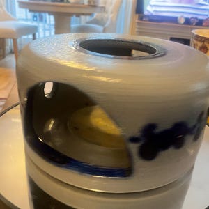 May include: A ceramic candle holder, cylindrical in shape, with a large opening at the top. The candle holder is light blue with dark blue floral designs and a dark blue rim. It sits on a mirrored surface.