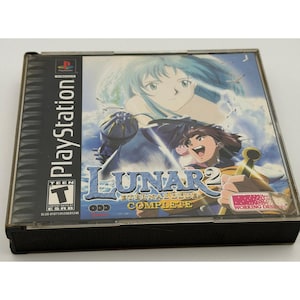 以下が含まれることがあります： 「Lunar 2: Eternal Blue Complete」のPlayStationゲームケース。表紙には、青と金のアクセントが施されたキャラクターのアニメ風イラストが描かれています。ゲームケースは、PlayStationのロゴが入った透明なプラスチックケースに入っています。