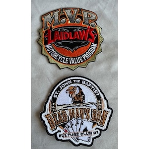 May include: Two embroidered patches. The top patch is star-shaped with orange, black, and red text reading M.V.P. LAIDLAWS MOTORCYCLE VALUE PROGRAM. The bottom patch is circular with a vulture illustration, playing cards, and text reading ST. JOHN THE BAPTIST DEAD MAN'S RUN VULTURE CLUB 07.