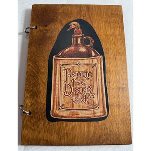 May include: Wooden journal with a dark brown stain. The cover features a graphic of a brown jug with the text "People I've Drunk With" in a vintage style. The journal is bound with two silver metal rings.