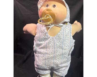 Bambola vintage Cabbage Patch Kids, neonato calvo con tutina blu a fiori e cappellino, anni '80.