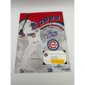 May include: A 2002 Chicago Cubs spring training program featuring a baseball player in a pinstripe uniform holding a bat. The cover includes the text 2002 SPRING PROGRAM, a blue ink autograph, the Cubs logo, and a business card for Harry Minor.