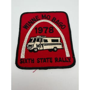 May include: A rectangular embroidered patch with a red background and black border. It features a white arch, a white recreational vehicle with the text WIT, the year 1978, and the text WINNE MO BAGO and SIXTH STATE RALLY in black embroidery.