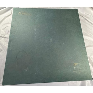 Pode incluir: Um jogo de tabuleiro Scrabble com uma superfície verde. A palavra "Scrabble" é impressa em dourado no canto superior esquerdo. O tabuleiro tem algumas manchas e marcas. O tabuleiro do jogo é quadrado e parece ser feito de cartão.