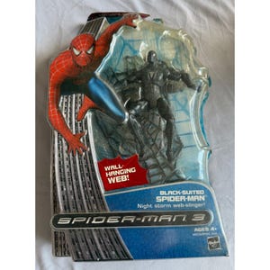 May include: A Spider-Man 3 action figure in original packaging featuring a black-suited Spider-Man figure, a red and blue Spider-Man graphic, and text including WALL-HANGING WEB, BLACK-SUITED SPIDER-MAN, and Night storm web-slinger.