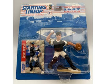 May include: A 1997 Starting Lineup Jason Kendall baseball action figure in original packaging. The figure wears a black and white uniform, holding a baseball and glove. The card features the text Starting Lineup 10th Year 1997 Edition.
