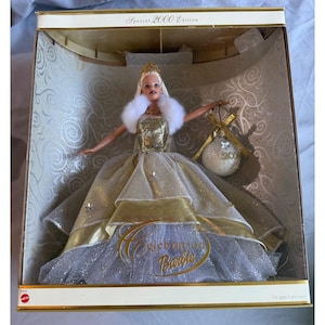 May include: A Barbie doll in a box, the Special 2000 Edition. The doll wears a gold and silver gown with a white fur stole and a crown. She holds a Christmas ornament with "2000" on it. The box reads "Celebration Barbie".