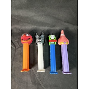 May include: Four colorful PEZ dispensers featuring popular characters. Includes a red Muppet, a gray bat, a green Thomas the Tank Engine, and a pink starfish. Each dispenser has a unique head design and a rectangular base.