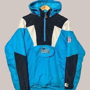 May include: Carolina Panthers anorak jacket in blue, black, and white. The jacket features a hood, a half-zip closure, and the NFL and Starter logos. The front pocket displays the Panthers logo. A vintage, retro-style windbreaker.