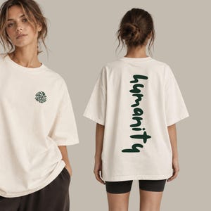 Könnte beinhalten: Ein cremefarbenes Oversize-T-Shirt mit einer kleinen runden schwarzen Grafik auf der Vorderseite mit dem Text "WEAR WHAT MATTERS" und einem großen vertikalen dunkelgrünen Schriftzug "humanity" auf der Rückseite in einer fetten Schreibschrift.