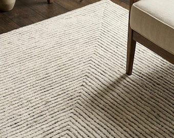 May include: A rectangular area rug featuring a textured, off-white and dark gray geometric pattern of concentric nested squares. The rug has a high-low pile construction that creates a distinct linear, ribbed effect across the entire surface.