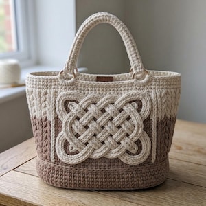 Può includere: Una borsa all'uncinetto bicolore con una sezione superiore color crema e una sezione inferiore marrone chiaro. La parte anteriore è decorata con un prominente motivo a nodo celtico in rilievo color crema. Include due manici robusti con anelli dorati.