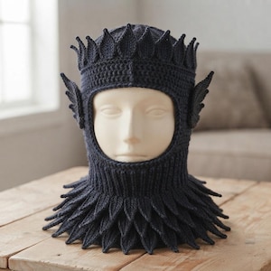 May include: A dark navy blue crochet balaclava featuring a crown-like top edge with pointed leaf-shaped details, matching leaf-shaped side accents, and a layered, petal-like collar that flares out around the neck area, covering the head and neck.