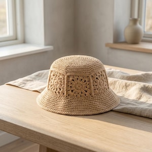 May include: A beige crochet bucket hat with a floral design. The hat is made of a woven material and has a wide brim. The hat is sitting on a wooden table.