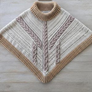 Peut inclure: Un poncho en tricot de couleur crème doté d'un col roulé côtelé et d'un ourlet côtelé assorti. Le vêtement présente un motif texturé de mailles torsadées verticales et diagonales dans une teinte beige clair, créant un design structuré.