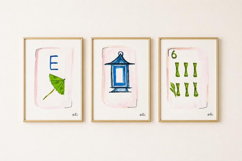 May include: Three framed watercolor prints with gold frames. Each print features a design on a white background with a pink wash. The designs include a blue letter "E" and green umbrella, a blue lantern, and the number "6" with green bamboo.
