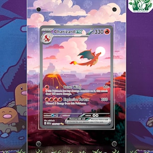 May include: A Charizard EX Pokémon card, stage 2, with a fiery orange dragon illustration, set against a landscape of mountains and a volcano. The card is encased in a clear display. Text includes "Brave Wing" and "Explosive Vortex".