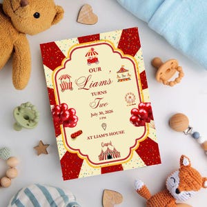 May include: A birthday invitation with a circus theme. The invitation is cream-colored with a red and yellow border and features circus-themed illustrations and the text "Our Liam's Turns Two". The invitation is surrounded by baby toys.