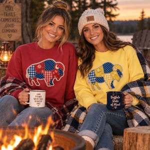 May include: A red sweatshirt with a patchwork buffalo graphic and a yellow sweatshirt with a patchwork buffalo graphic. The red sweatshirt is paired with a white mug featuring the text Good Friends Warm Fires Brighter Days. The yellow sweatshirt is paired with a dark blue mug featuring the text Buffalo State of Mind.