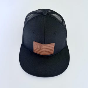 Cappellino da camionista nero con visiera piatta e profilo alto, con bandiera degli Stati Uniti.