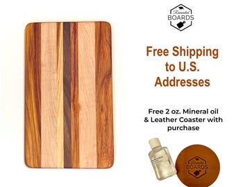 May include: A rectangular wooden cutting board featuring vertical stripes of light, medium, and dark brown wood grain. Included is a small clear bottle of 2 oz. mineral oil and a round brown leather coaster with a logo.