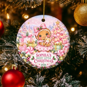 May include: A round ceramic Christmas ornament featuring a gingerbread character with a pink bow holding a small cat, surrounded by gifts, a pink Christmas tree, and candy. The text reads: SOPHIA'S MERRY LITTLE CHRISTMAS 2026 in red and green.