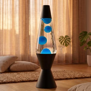 May include: A black and clear lava lamp with blue wax. The lamp has a black base and top, with a clear glass container holding the blue wax. The lamp is on a wooden floor, with a woven rug and pillows in the background.