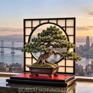 Könnte beinhalten: Ein schwarzer quadratischer Rahmen mit kreisförmigem Ausschnitt und Gittermuster sowie einer roten Basisplattform. Der Rahmen ist für die Präsentation eines Bonsai-Baums konzipiert. Der Text "BONSAI NOT INCLUDED" steht unten im Bild.