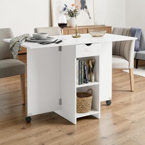 May include: A white drop-leaf table with a central storage unit featuring a drawer, two open shelves, and wheels. The top shelf holds three books titled Gastronomy, Tastes, and Craft Cocktails, while the bottom shelf contains a woven wicker basket.