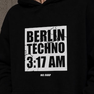 May include: Black hoodie with the text "BERLIN TECHNO 3:17 AM" in a white, cracked font. The phrase "NO SLEEP" is below the main text. The hoodie has a hood and a simple design.