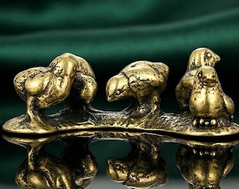May include: A small, antique-style brass sculpture featuring three stylized bird figures. The birds are perched on a connected base, with a reflective surface below. The sculpture has a weathered, aged appearance, suggesting it is a vintage or antique item.
