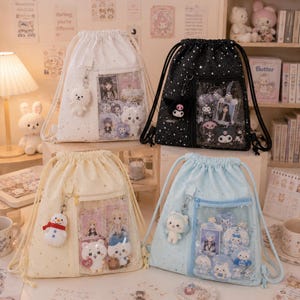 Puede incluir: Cuatro mochilas con cordón en blanco, negro, amarillo y azul claro, cada una con un bolsillo transparente que muestra pequeñas figuras y tarjetas. Cada bolsa tiene un llavero de peluche a juego. Las bolsas están decoradas con patrones de estrellas.