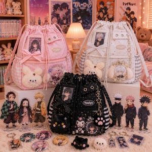 May include: Three drawstring backpacks in pink, white, and black, each with decorative elements like plush animals, bows, and character portraits. The black bag has a star and paw charm. Various character figurines and keychains are displayed in front.