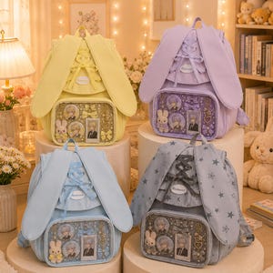 Puede incluir: Cuatro mochilas con largas orejas de conejo, detalles de cintas entrelazadas y un bolsillo frontal transparente lleno de pines decorativos, dijes y pequeños peluches. Las mochilas vienen en colores amarillo, morado claro, azul claro y gris con estrellas.