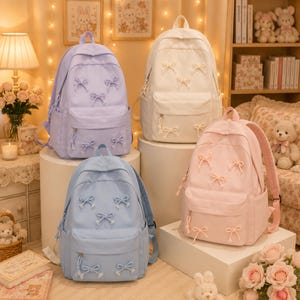 May include: Four backpacks in pastel colors including lavender, white, light blue, and soft pink. Each backpack features a main compartment, a front zippered pocket, and multiple small decorative bows attached to the exterior fabric surface.