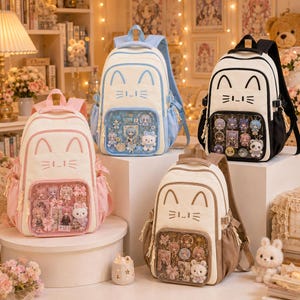 May include: Four backpacks featuring cat-ear designs and clear front pockets filled with various character pins and plush charms. The backpacks come in light blue, black, pink, and beige, each with embroidered cat faces and side pockets.
