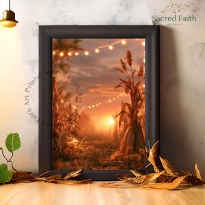 May include: A black rectangular frame containing an art print of a cornfield at sunset. The scene features tall corn stalks, golden light, and a string of glowing fairy lights against a warm orange sky. The text Sacred Faith Art Prints is visible.