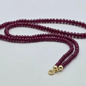 Può includere: Una collana composta da piccole perline rotonde, rosso scuro. Le perline sono infilate insieme, formando un anello continuo. La collana ha una chiusura dorata.