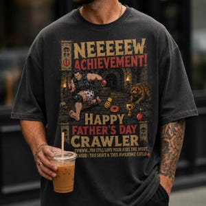 Könnte beinhalten: Dunkelgraues T-Shirt mit dem Aufdruck "NEEEEEW ACHIEVEMENT! HAPPY FATHER'S DAY CRAWLER" und einer Cartoon-Grafik. Die Grafik zeigt eine muskulöse Figur, einen Löwen und verschiedene Objekte. Das T-Shirt hat eine lockere Passform.