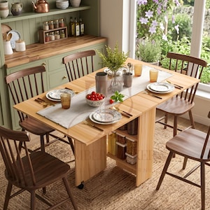 May include: A light wood drop-leaf dining table set for a meal, surrounded by wooden chairs and a woven rug. The table is set with plates, glasses, and cutlery. A vase of greenery and a bowl of tomatoes are on the table. The table is approximately 150 cm long.