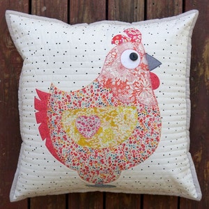 May include: A white pillow with a black polka dot pattern features a colorful patchwork chicken applique. The chicken is made of various floral fabrics in shades of red, pink, yellow, and green. The chicken has a large button eye and a gray beak.