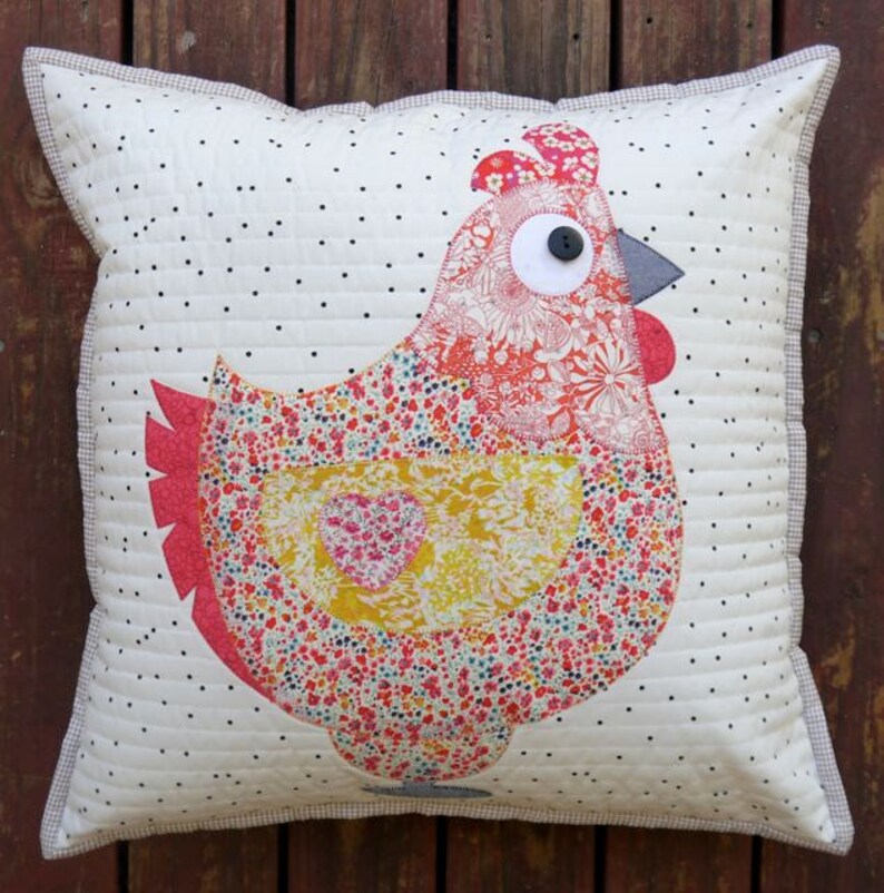 May include: A white pillow with a black polka dot pattern features a colorful patchwork chicken applique. The chicken is made of various floral fabrics in shades of red, pink, yellow, and green. The chicken has a large button eye and a gray beak.