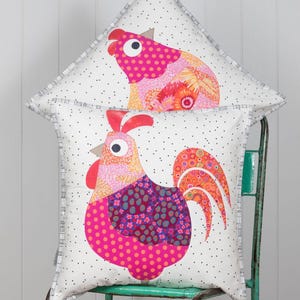 May include: Two decorative throw pillows with a white background and a black polka dot pattern. The pillows feature a colorful rooster design with pink, orange, and purple accents.