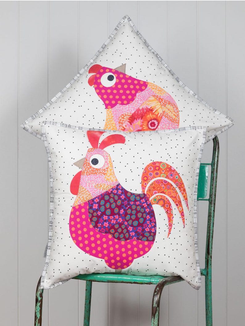 May include: Two decorative throw pillows with a white background and a black polka dot pattern. The pillows feature a colorful rooster design with pink, orange, and purple accents.