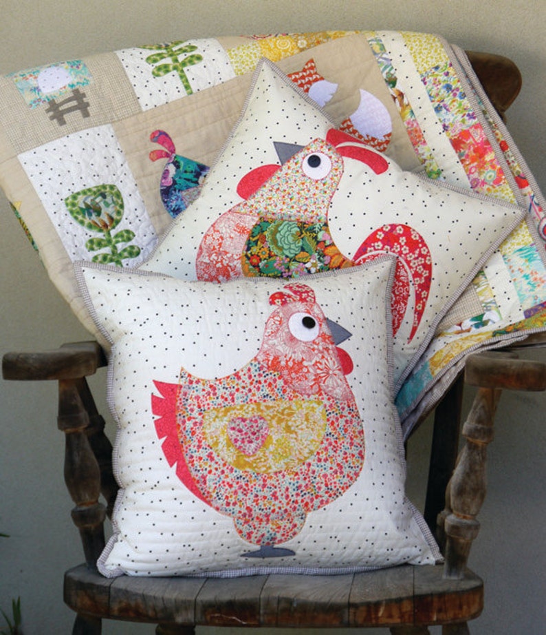 May include: Three decorative pillows featuring a rooster and two hens. The pillows are made of white fabric with black polka dots and feature colorful patchwork designs. The pillows are sitting on a wooden rocking chair.