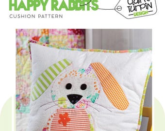 May include: A white cushion with a colorful patchwork design featuring a rabbit with a pink flower. The cushion is titled "Happy Rabbits Cushion Pattern" and is designed by Claire Turpin.