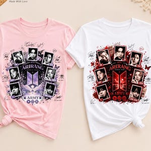 Op de afbeelding: Een lichtroze T-shirt en een wit T-shirt, elk met een grafische print van de BTS Arirang World Tour. De ontwerpen bevatten zeven individuele portretten van de bandleden, het BTS-logo en diverse handtekeningen in een cirkelvormig patroon.